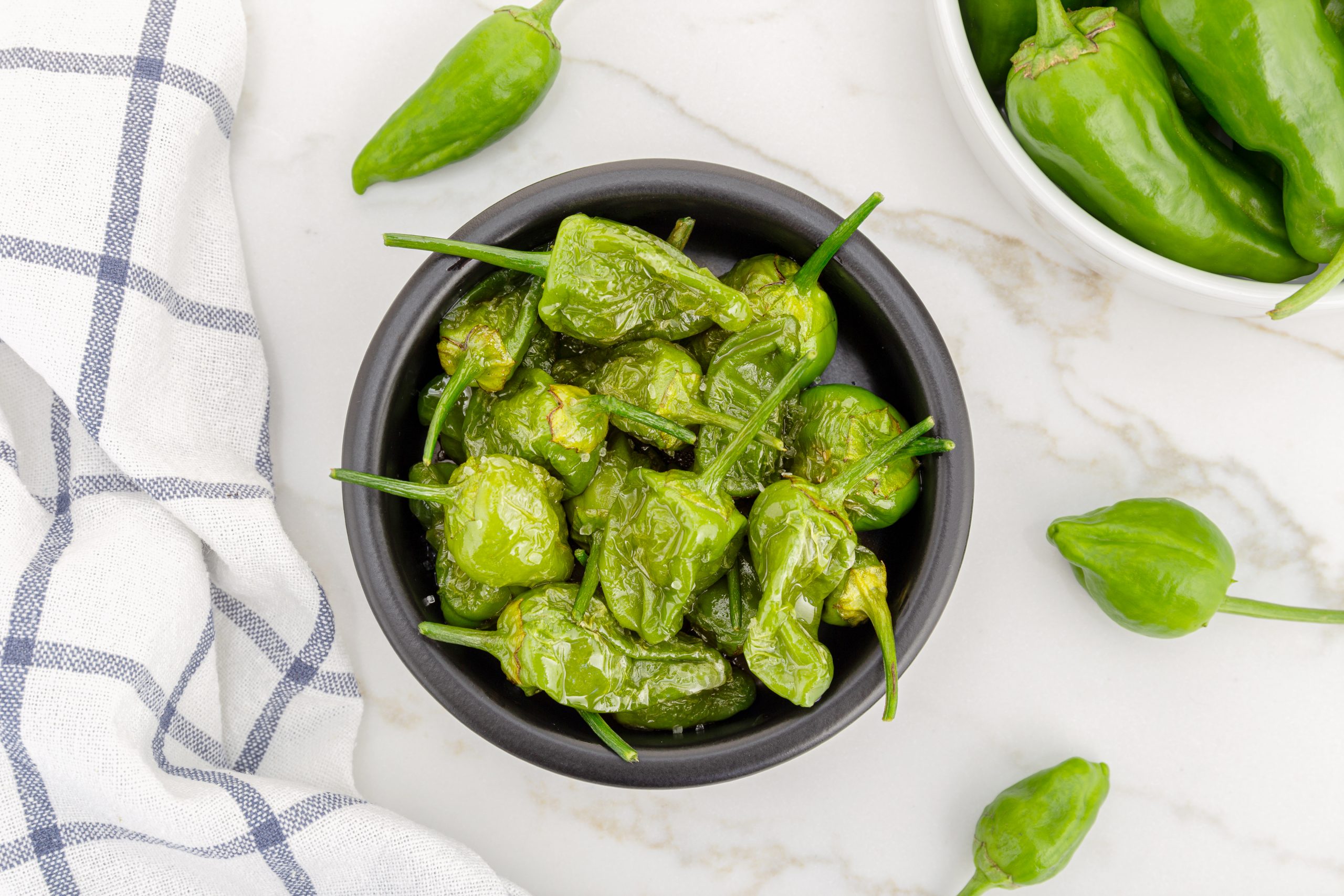 Top view of Cooked Padron peppers in a a bowl on marble table